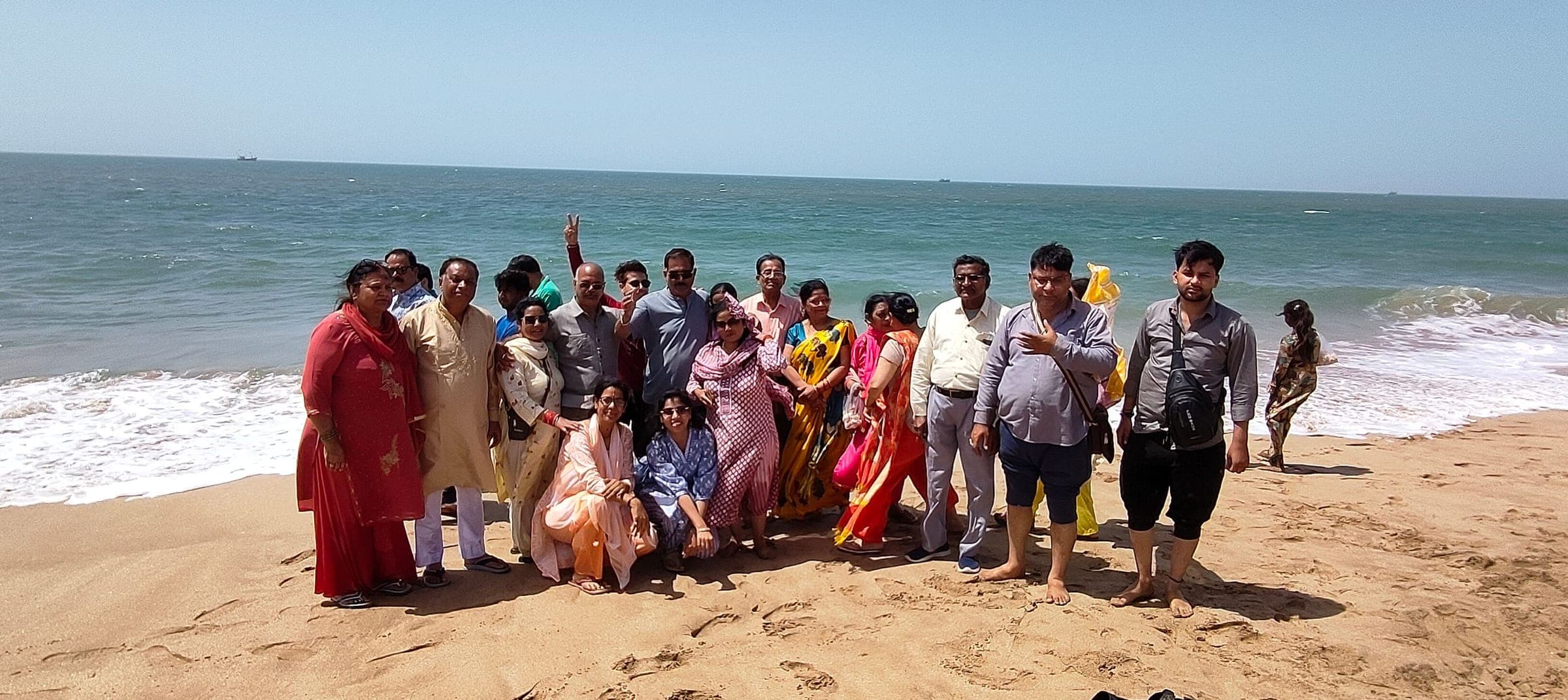 A large group of travellers gathered on a sandy beach, waves breaking behind them